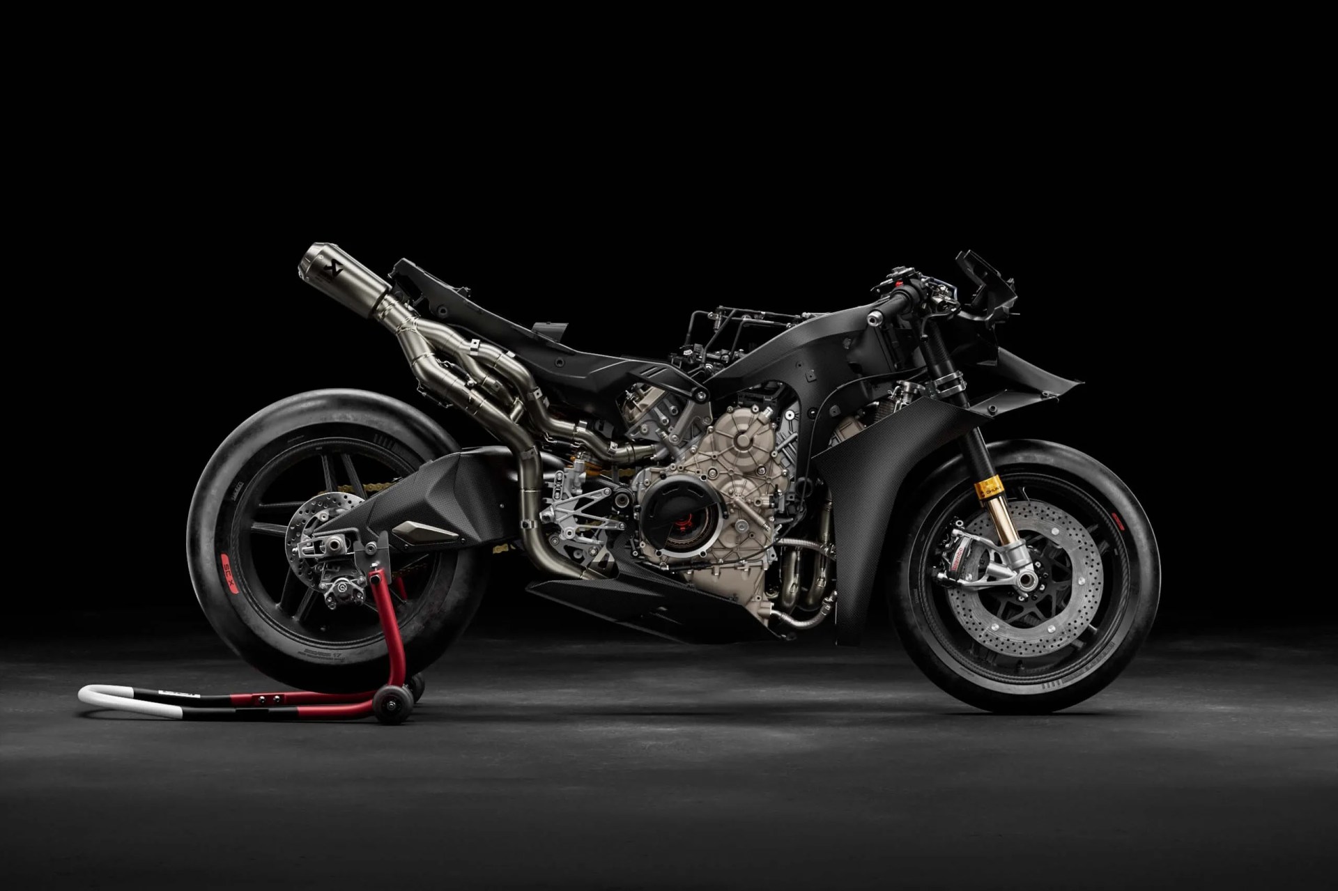 Black sport motorcycle frame with exposed engine and exhaust system on a rear stand against a black background.