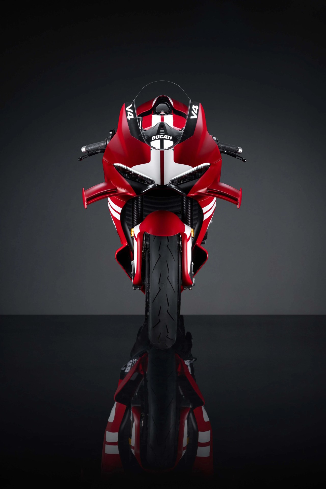 Red Ducati V4 sport motorcycle with white racing stripes, shown from the front on a reflective black surface.