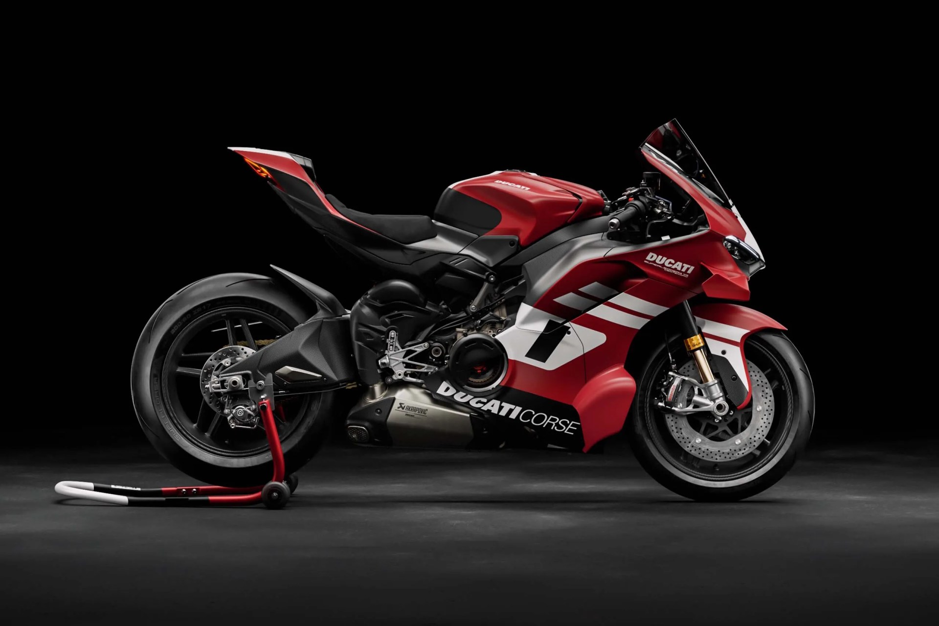 Red and white Ducati Corse sport motorcycle on a rear stand against a black background.