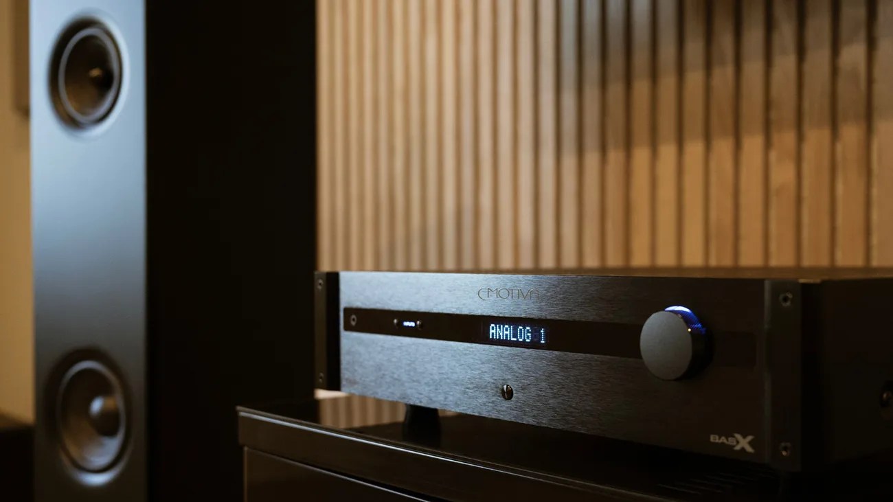 Black MOTIV BasX audio amplifier with digital display showing "ANALOG 1" next to a tall black speaker.