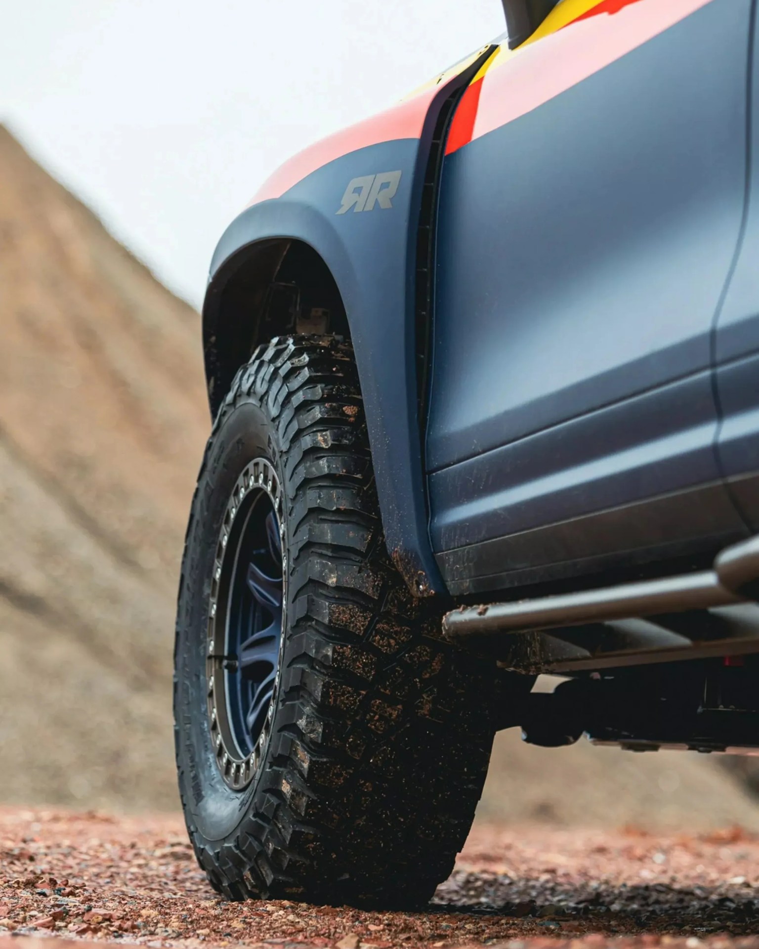 Close-up of a rugged off-road tire with deep treads on a blue vehicle with an "RR" logo on the fender.