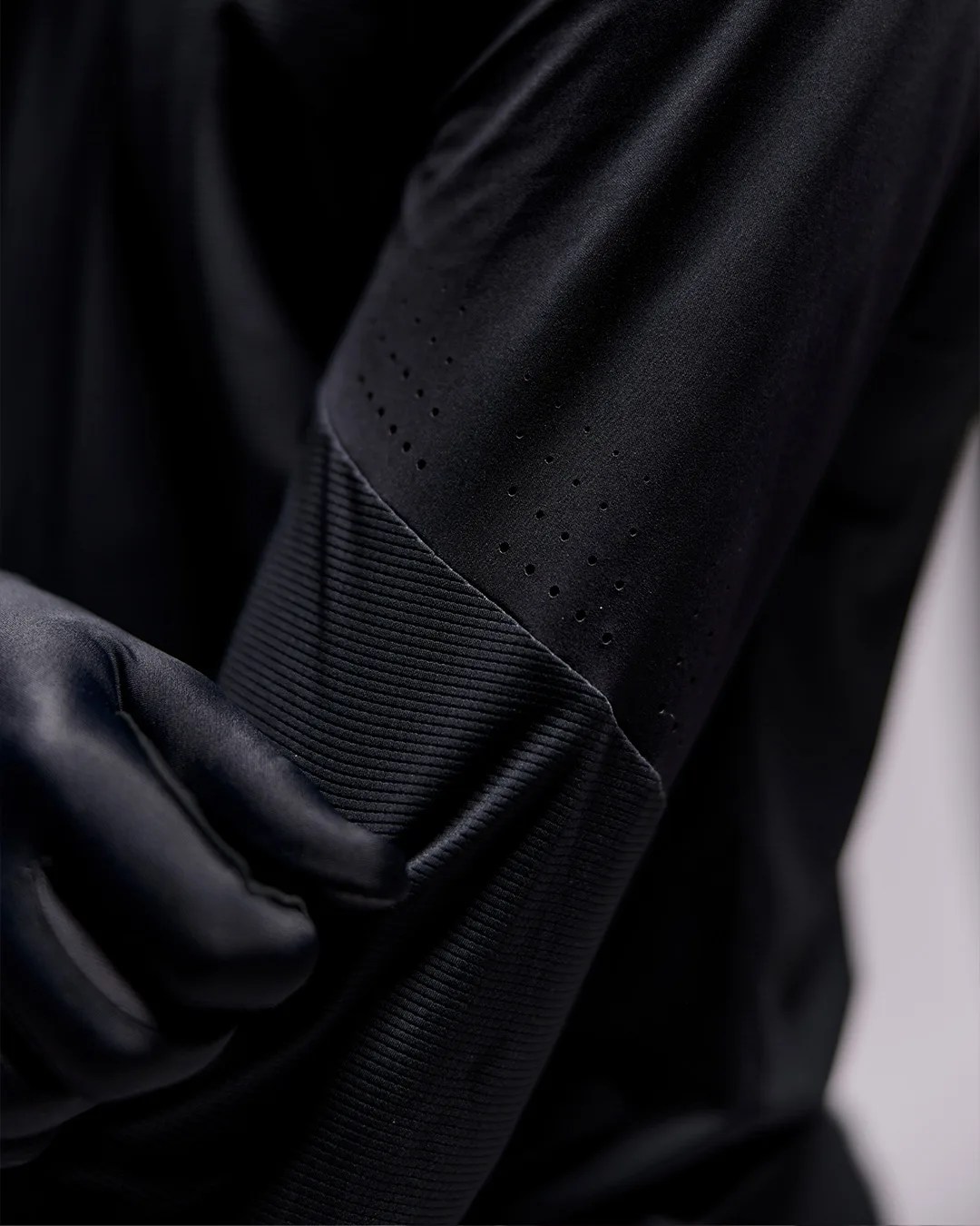 Close-up of a black long-sleeve garment with perforated details and ribbed cuff worn by a person.