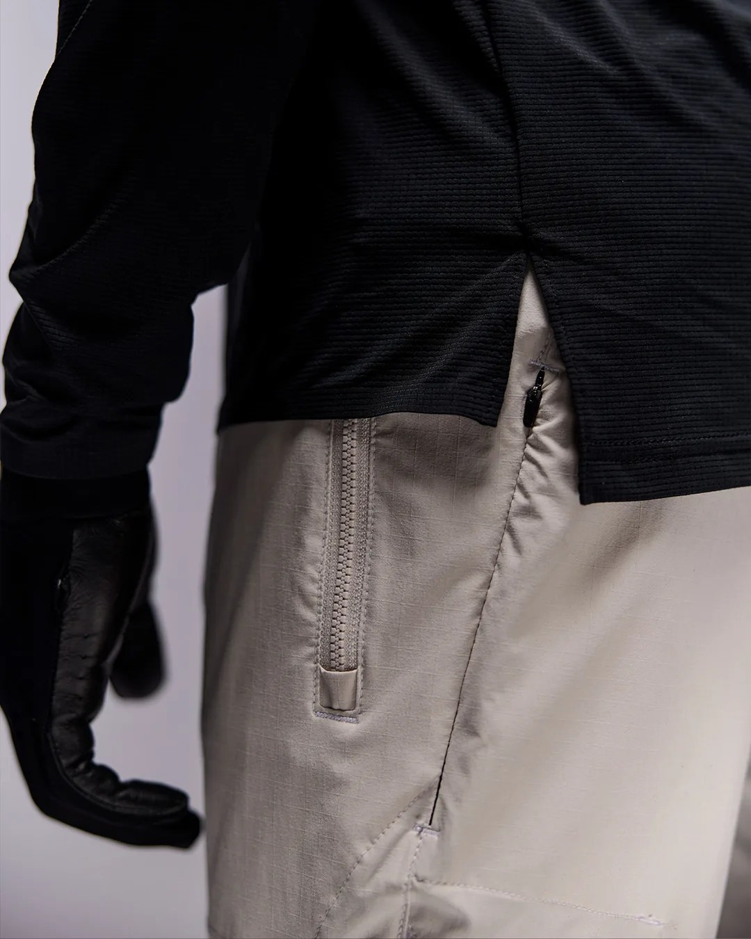 Close-up of beige pants with a vertical zipper pocket and a black textured top with a side slit.