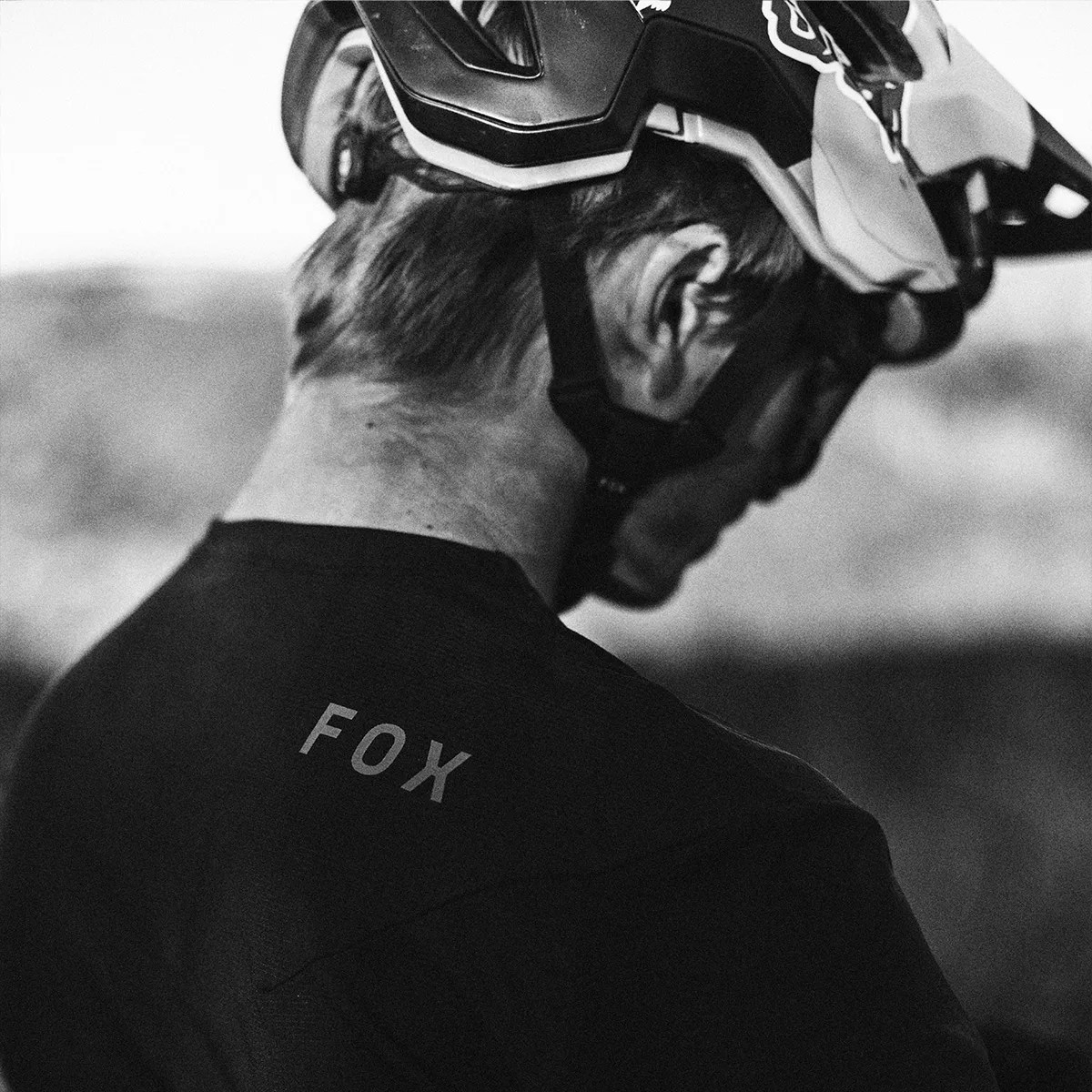 Person wearing a black shirt with "FOX" text on the back and a bike helmet worn backward.
