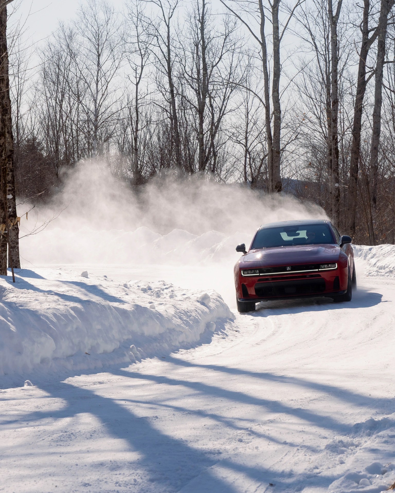 Red car drifting on a snow-covered road with snow and trees in the background.