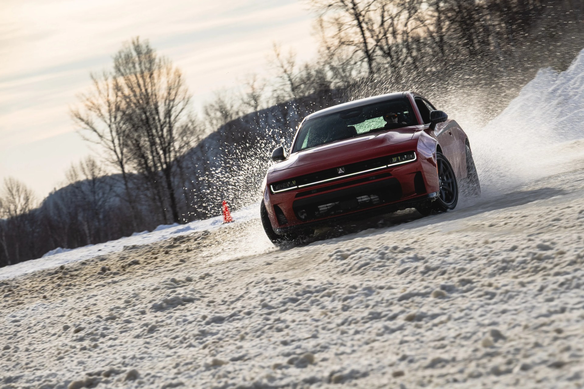 Red electric car drifting on a snowy road with snow spraying around it.