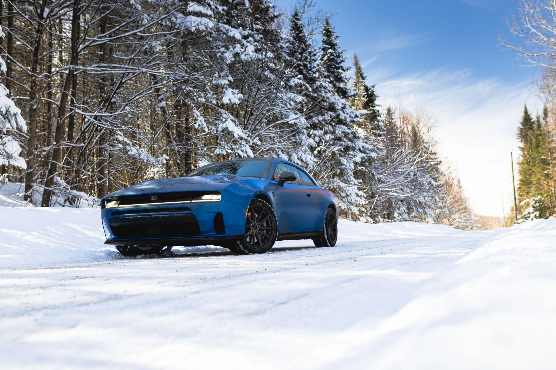 Blue sports car with black wheels parked on a snowy road surrounded by snow-covered trees.