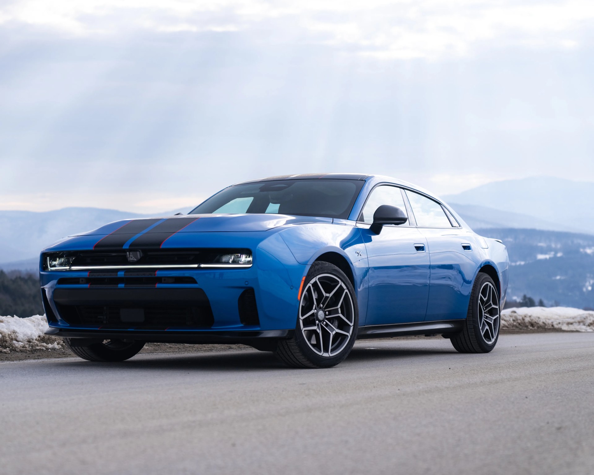Blue Dodge Charger with black and red racing stripes parked on a snowy mountain road.