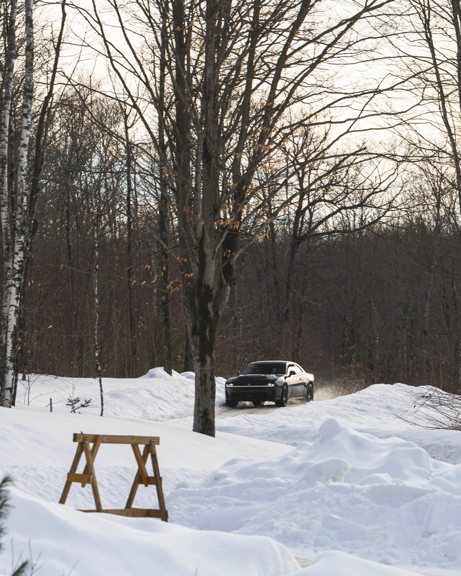 Black sports car driving on a snow-covered road through a leafless forest in winter.