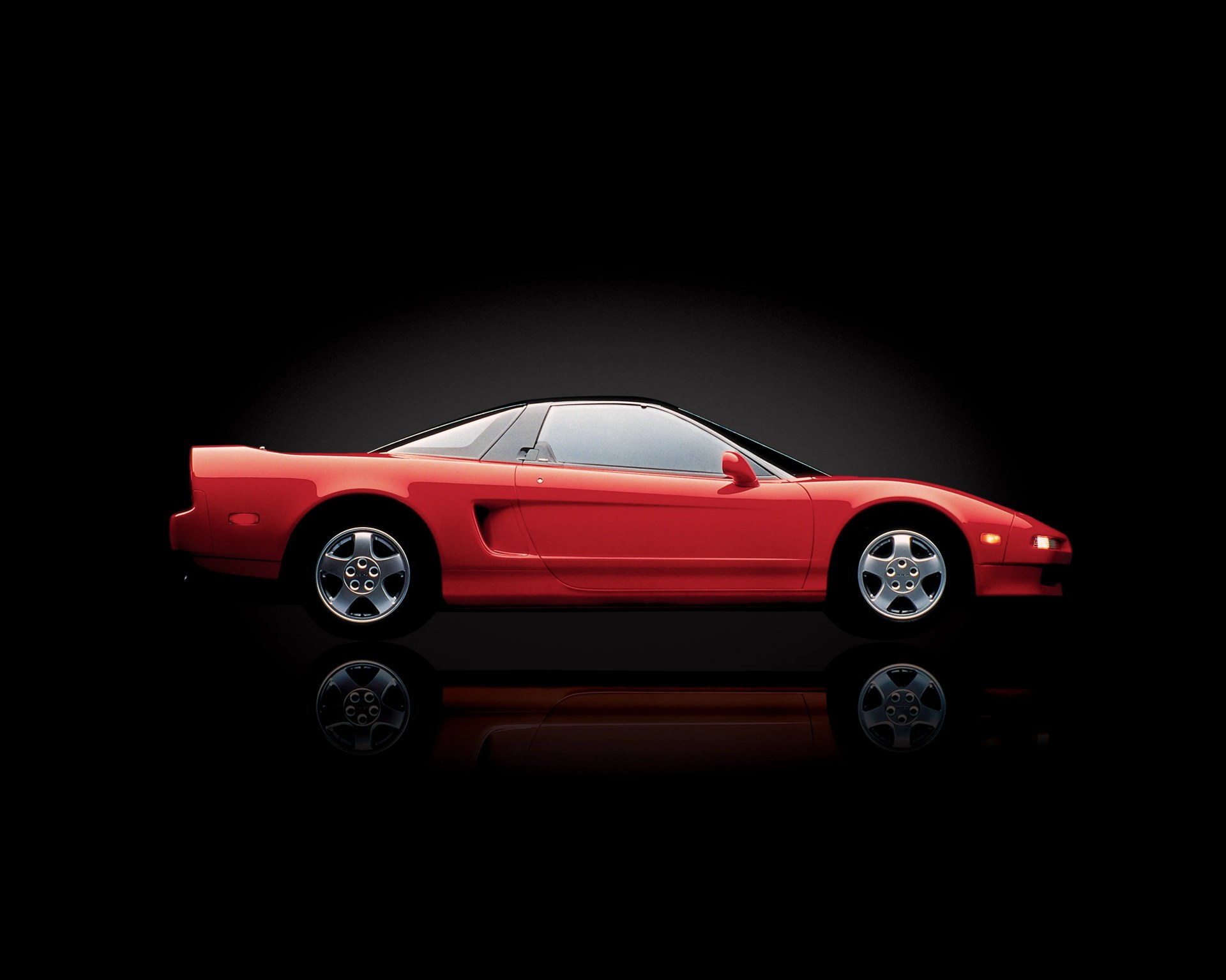 Red two-door sports car with silver wheels and black roof on a reflective black surface.