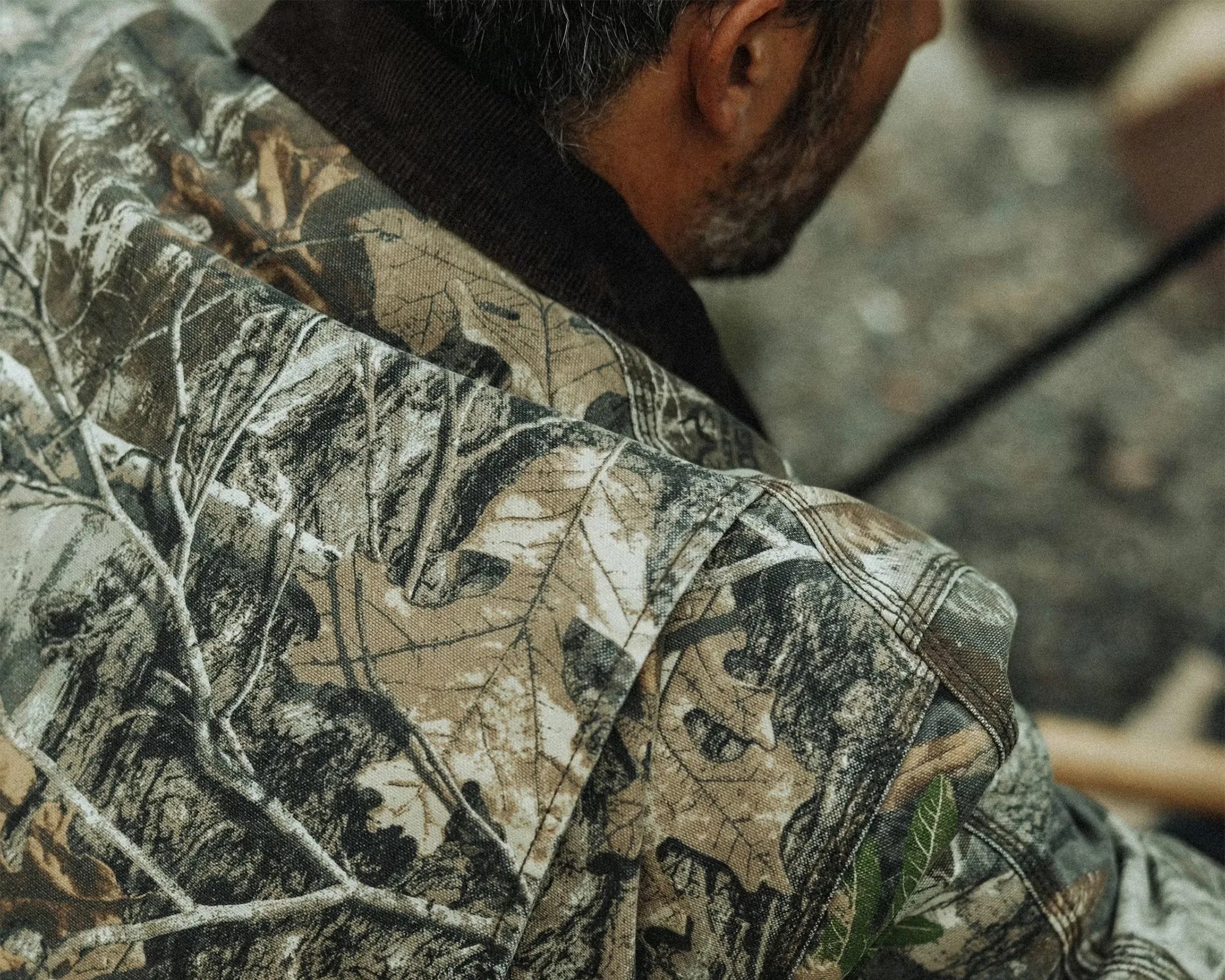 Close-up of a person wearing a camouflage jacket with a leaf and branch pattern.