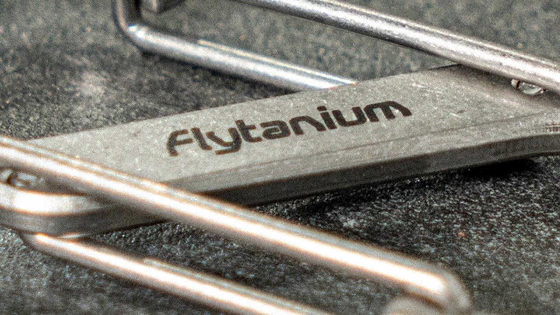 Close-up of a metal tool with "Flytanium" engraved on its surface, resting on a textured dark background.