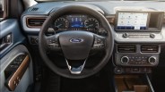 Black leather-wrapped Ford steering wheel with multifunction controls and digital instrument cluster behind it.