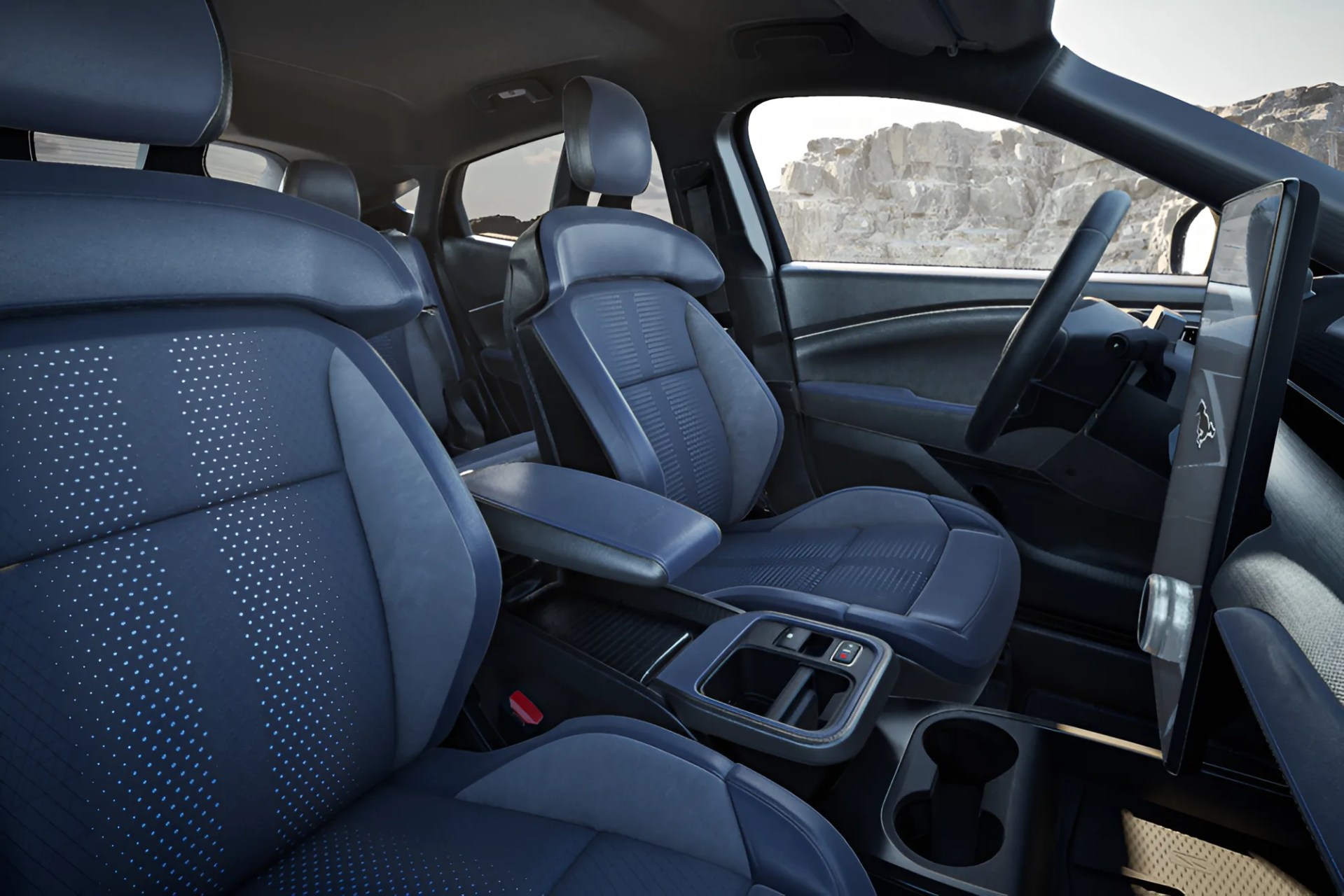 Interior of a car with blue perforated leather seats, a large vertical touchscreen, and a black steering wheel.