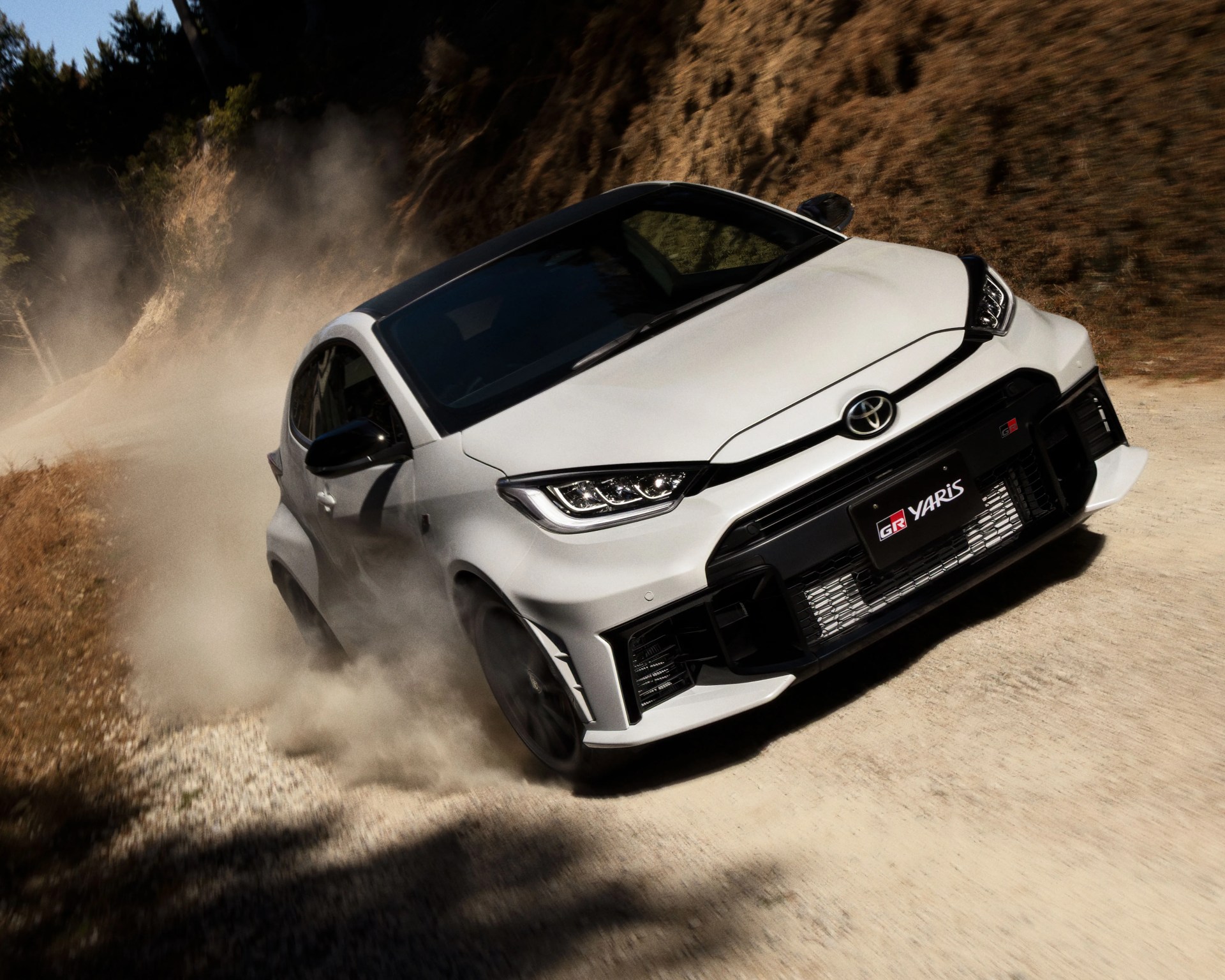 White Toyota GR Yaris with black roof drifting on a dusty gravel road.