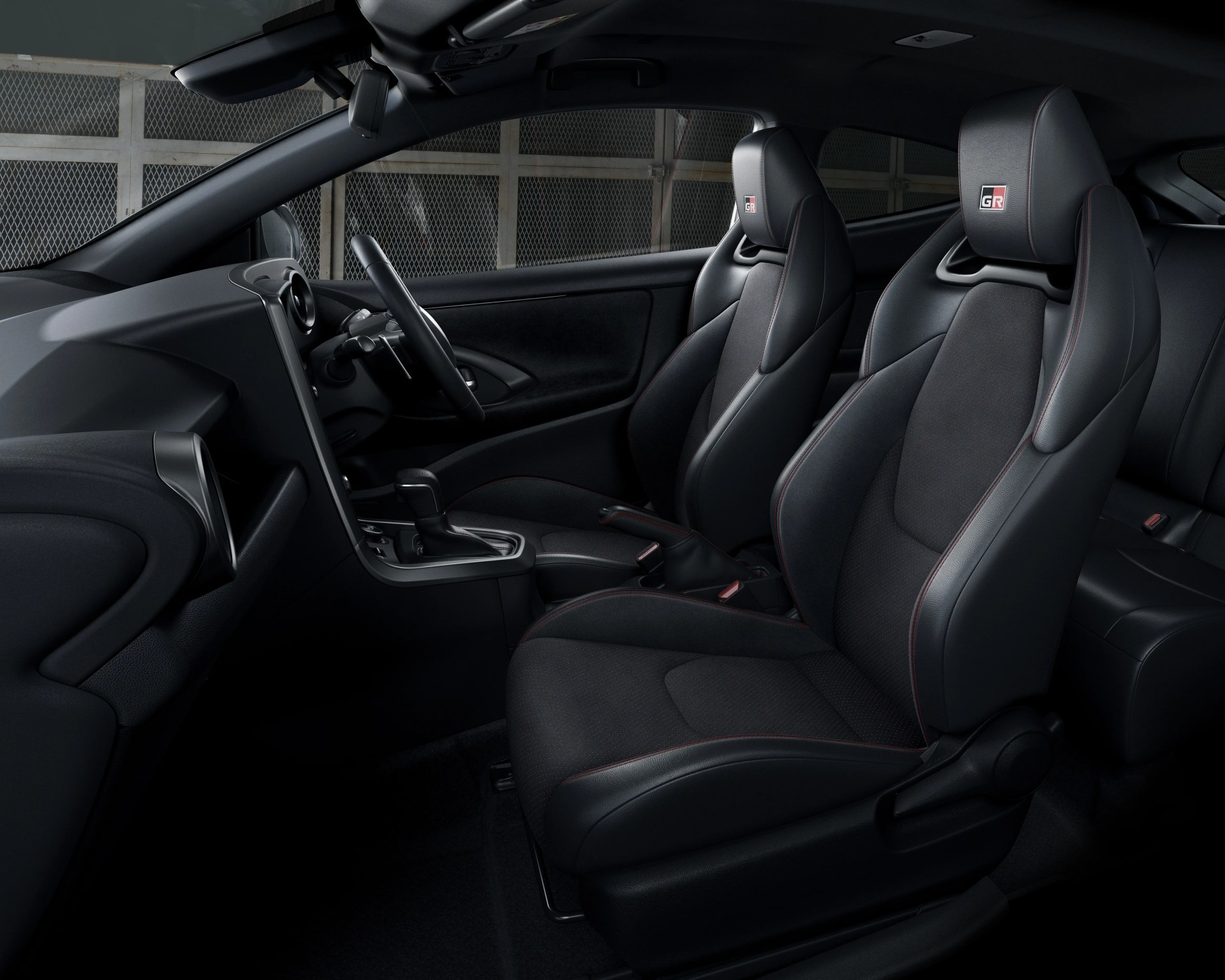 Two black sport seats with red stitching and GR logos on headrests inside a car interior.