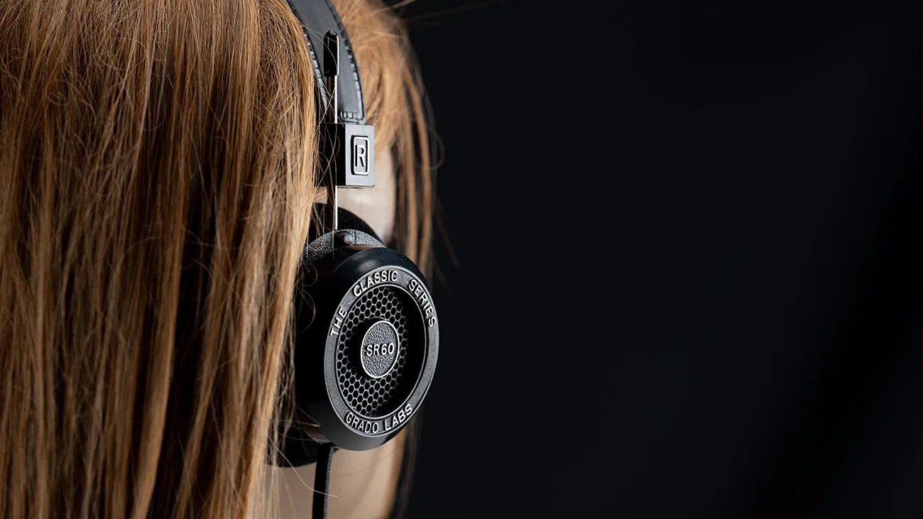 Black Grado Labs SR60 Classic Series headphones worn on a person with long brown hair against a dark background.