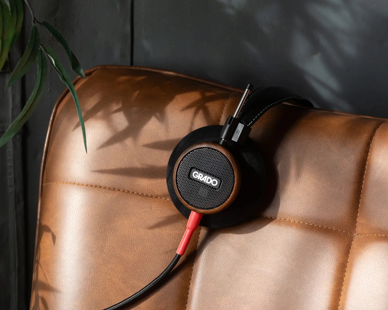 Black and wood Grado headphones with red cable resting on a brown leather chair.