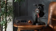 Black and copper Burson audio amplifier with digital display next to black and wood Grado headphones on a wooden table.