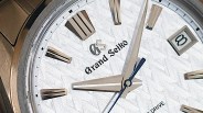 Close-up of a Grand Seiko watch face with silver hour markers, date window at 3 o'clock, and textured white dial.