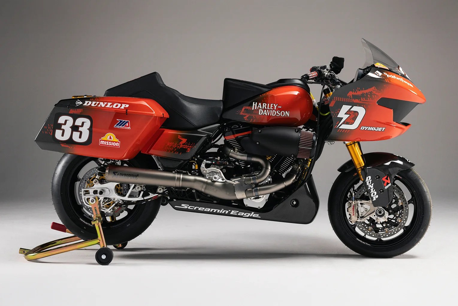 Red and black Harley-Davidson racing motorcycle with number 33 and sponsor logos on a rear stand.