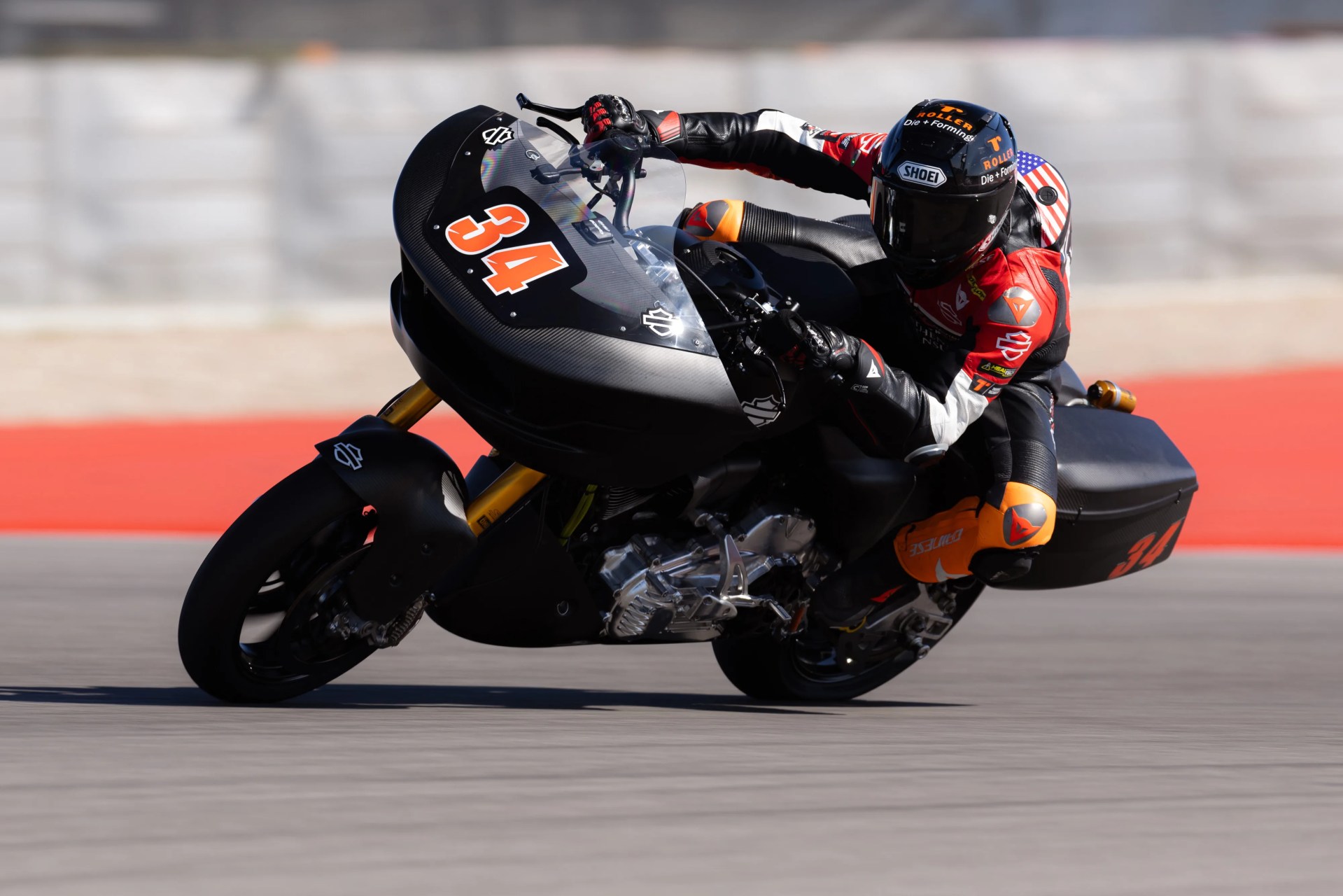 Motorcycle racer in black and red gear leaning into a turn on a black race bike numbered 34.