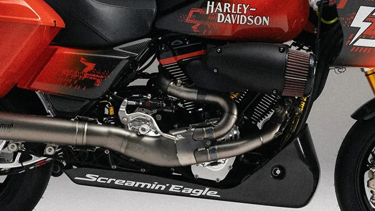 Close-up of a red Harley-Davidson motorcycle engine with black and silver exhaust pipes and "Screamin' Eagle" text on the lower fairing.