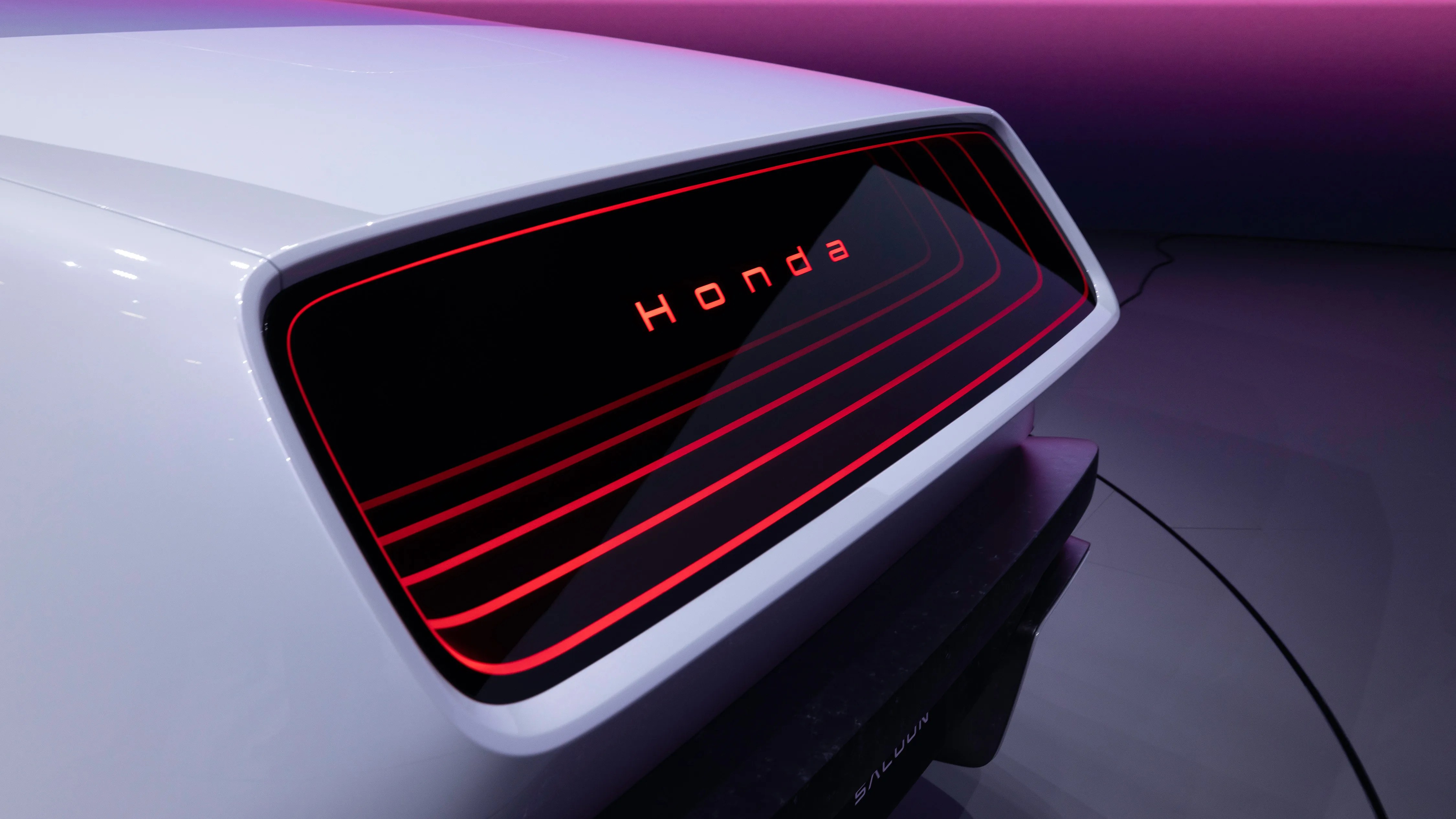 Rear view of a white Honda car with a black and red illuminated panel displaying the Honda logo.