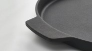 Close-up of a textured black cast iron skillet handle on a light surface.
