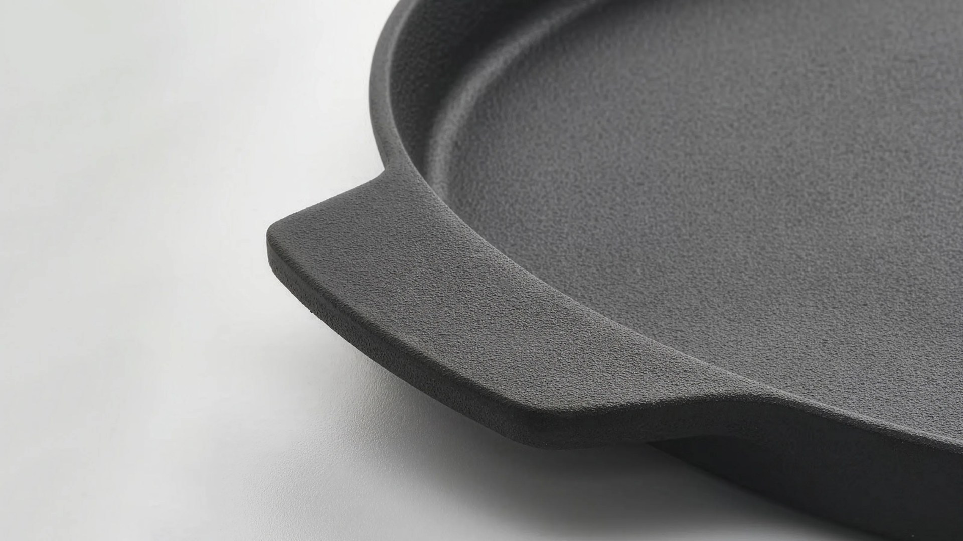 Close-up of a textured black cast iron skillet handle on a light surface.