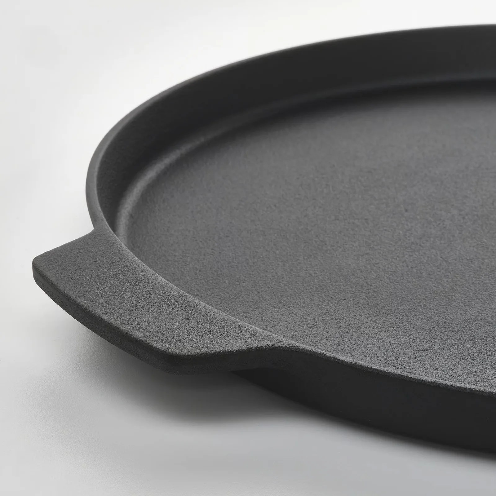 Close-up of a round black cast iron griddle pan with a flat handle on a white surface.