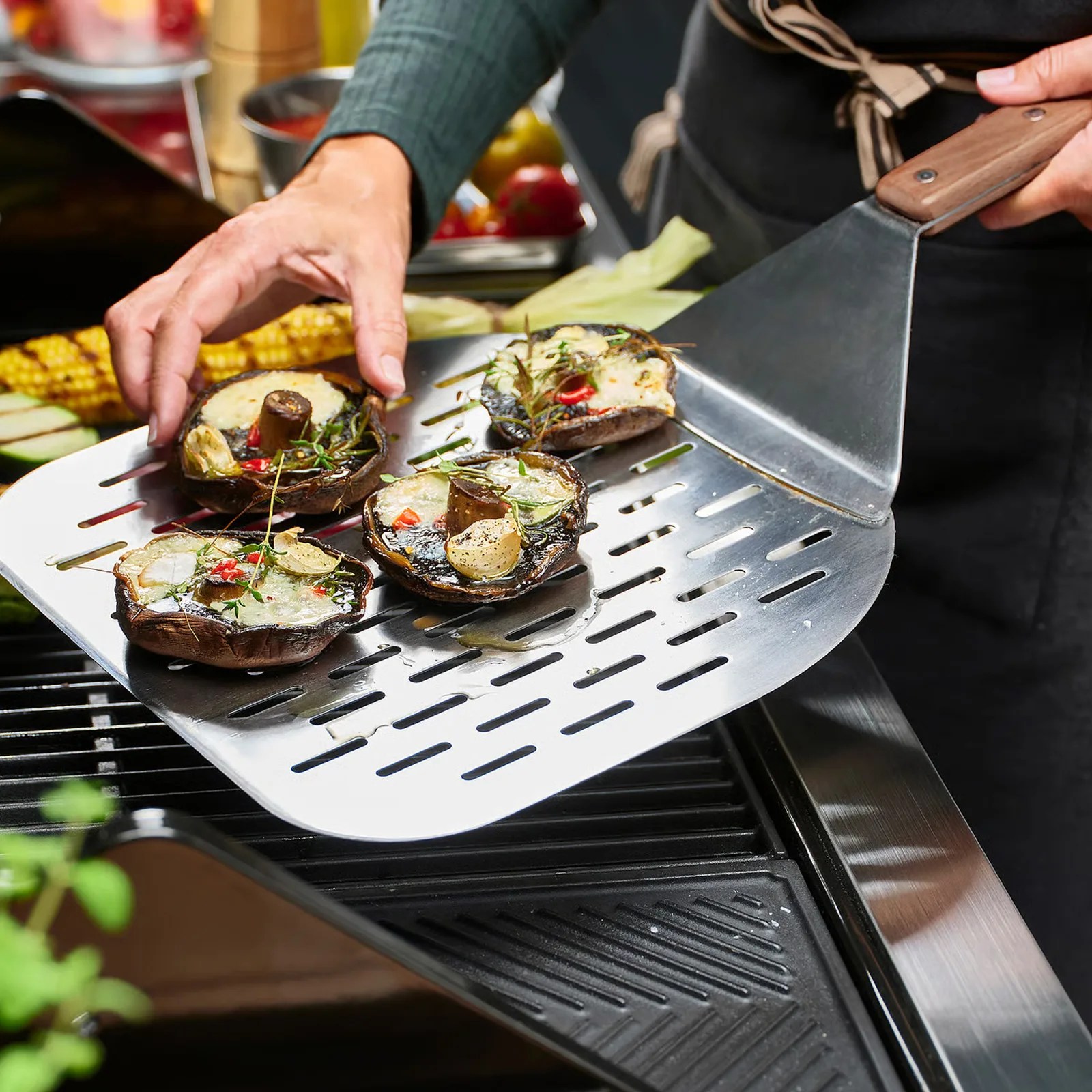 Grilled portobello mushrooms with herbs and garlic on a perforated stainless steel spatula over a grill.