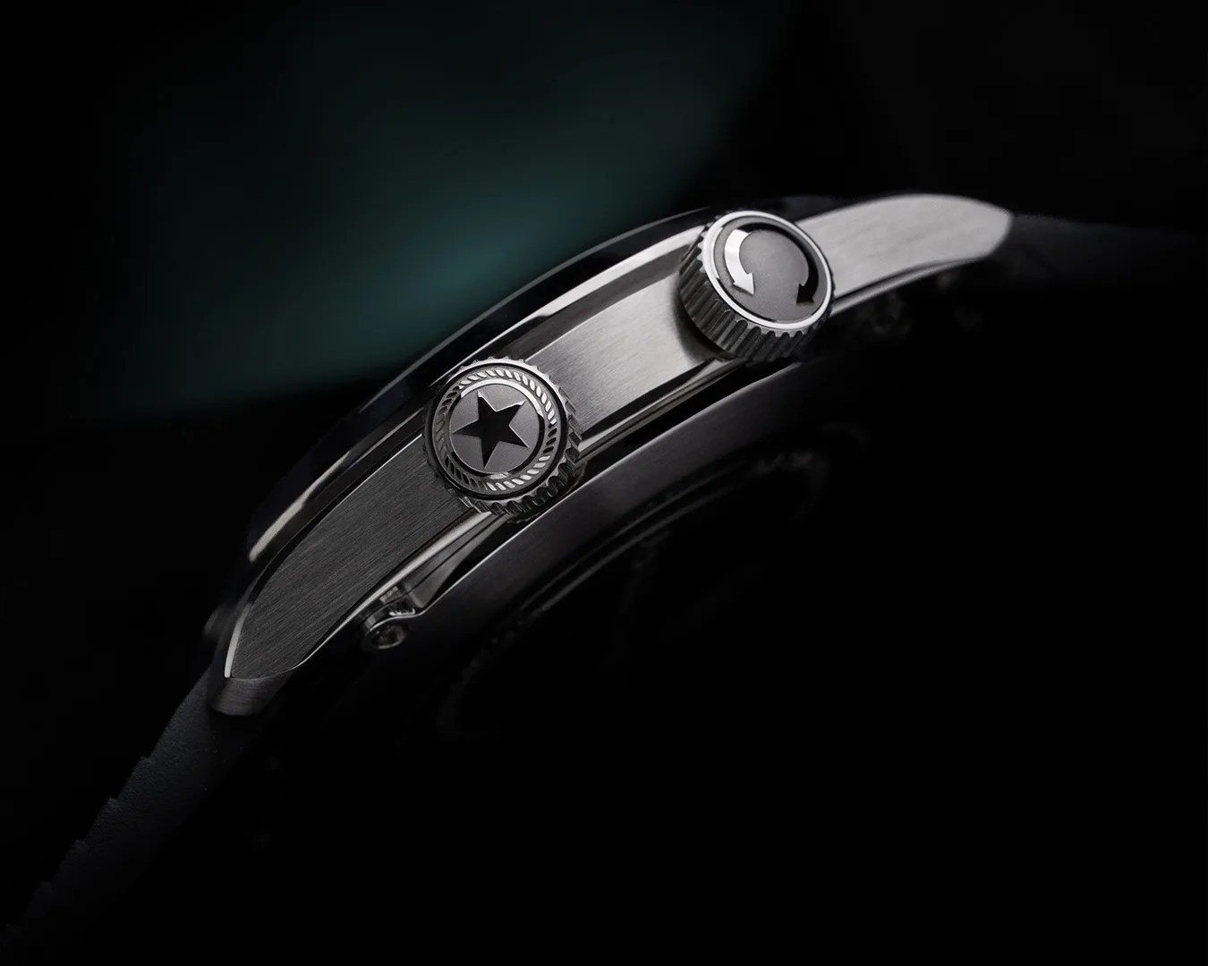 Close-up of a brushed stainless steel watch case side with two crowns, one featuring a star and the other a circular arrow symbol.