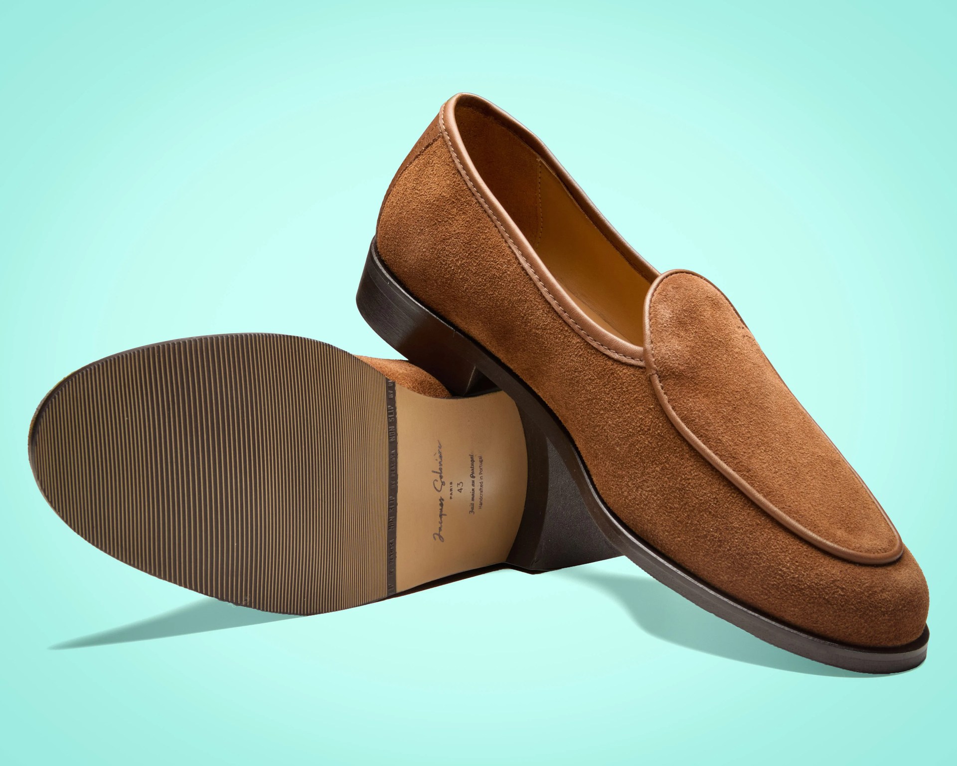 Pair of brown suede loafers with leather trim and rubber soles on a light blue background.