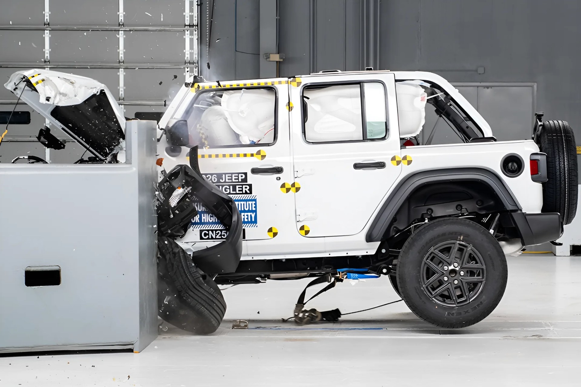 White Jeep Wrangler undergoing a frontal crash test with deployed airbags and impact damage.