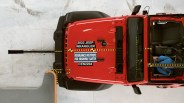 Top-down view of a red 2022 Jeep Wrangler undergoing a crash test with safety markings and a crash test dummy inside.