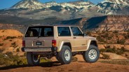 Beige Jeep Cherokee with off-road tires parked on rocky terrain with snow-capped mountains in the background.