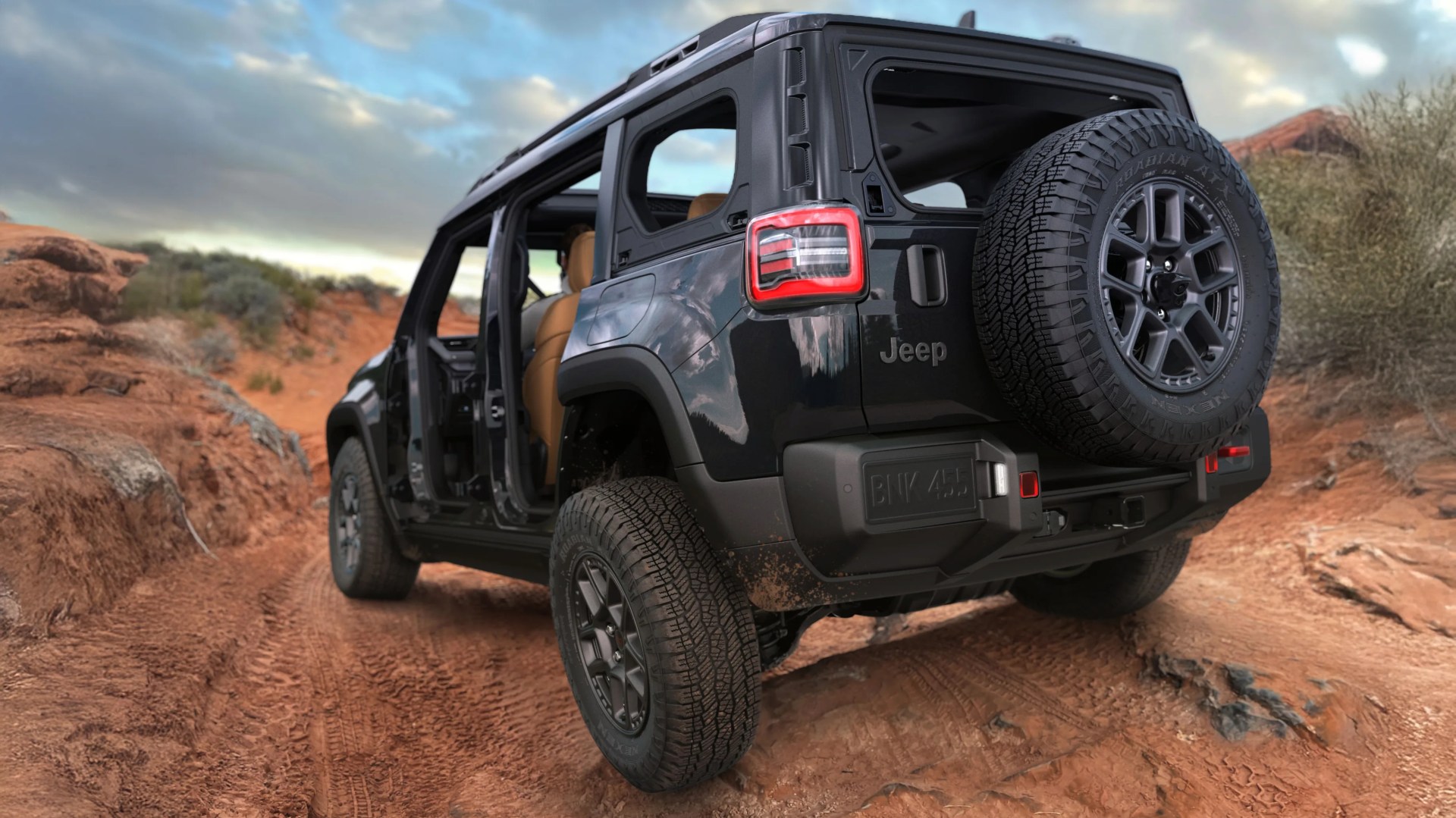 Black Jeep SUV with open doors and spare tire on rugged red dirt trail.