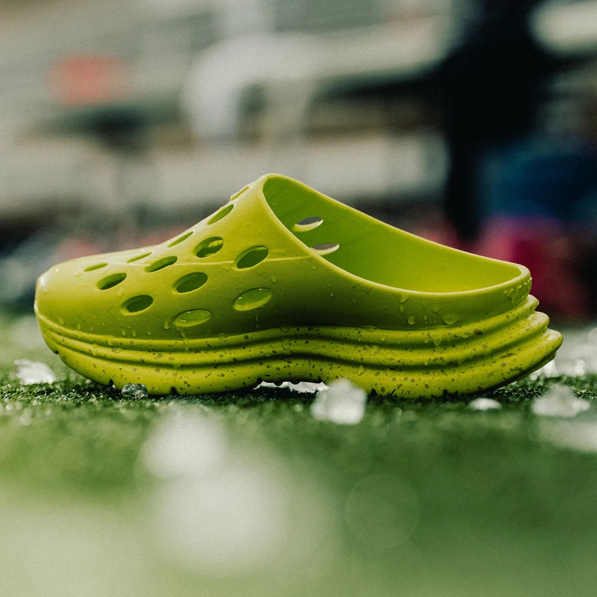 Bright green slip-on clog with multiple oval ventilation holes and a textured sole on grass.