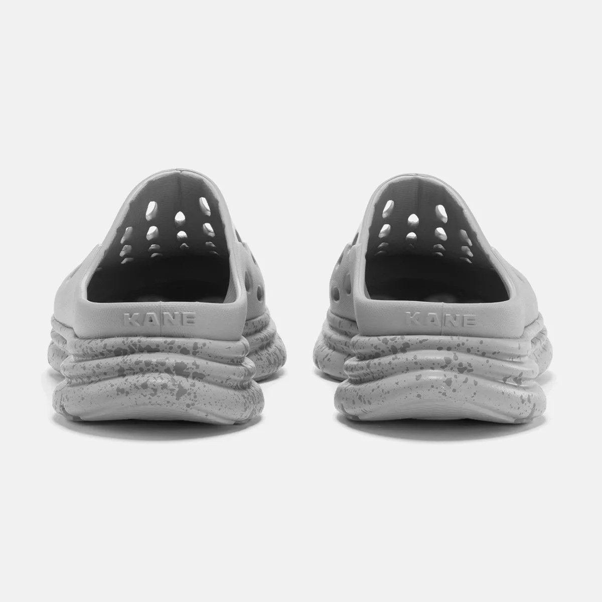 Pair of light gray slip-on shoes with perforated uppers and speckled, textured soles, viewed from the back.