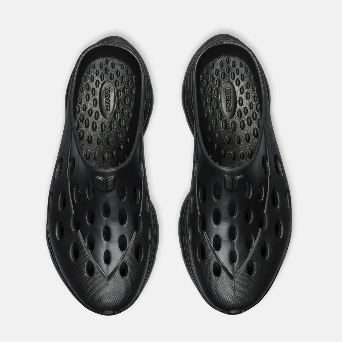 Pair of black slip-on shoes with multiple oval ventilation holes and textured insoles labeled "KANE.