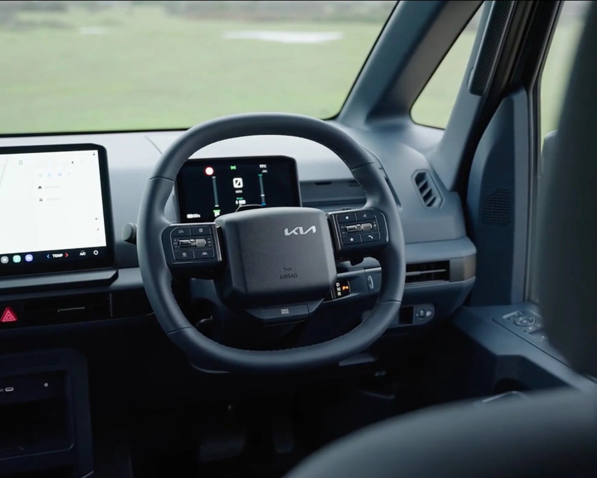 Black Kia steering wheel with control buttons and digital dashboard inside a car.