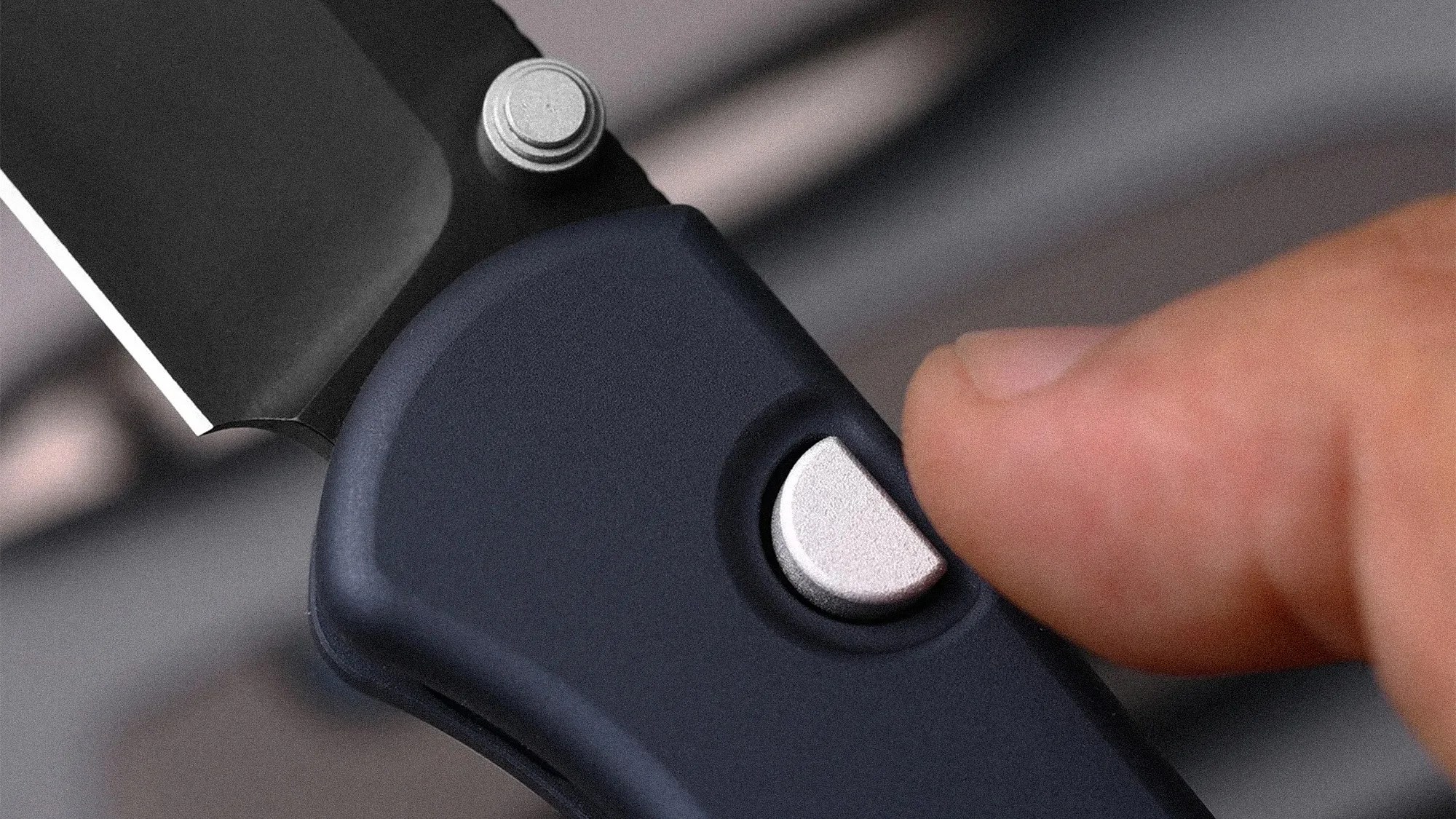Close-up of a finger pressing the silver button on a black folding knife handle near the blade pivot.