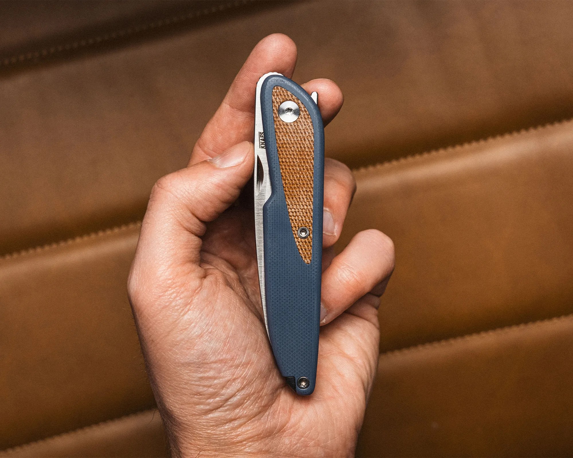 Hand holding a closed folding knife with a blue handle and brown textured inlay.