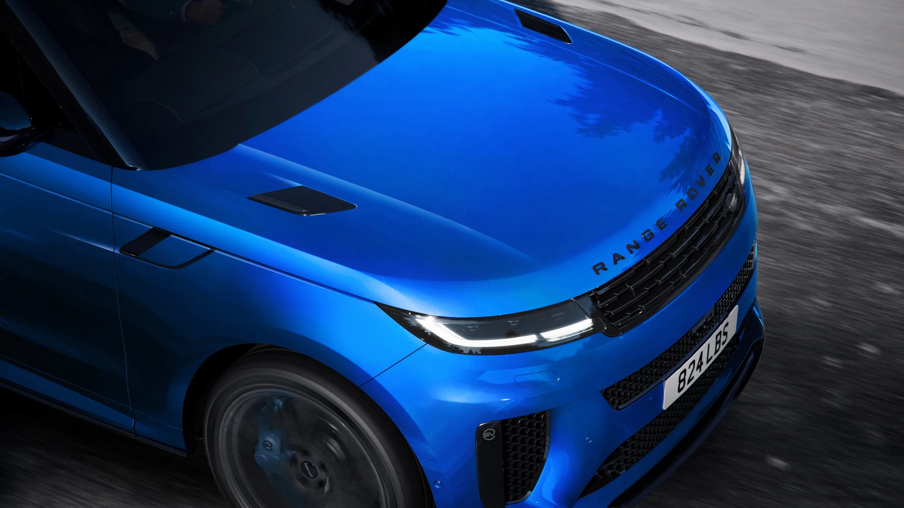 Front view of a blue Range Rover with illuminated headlights and black grille on a road.