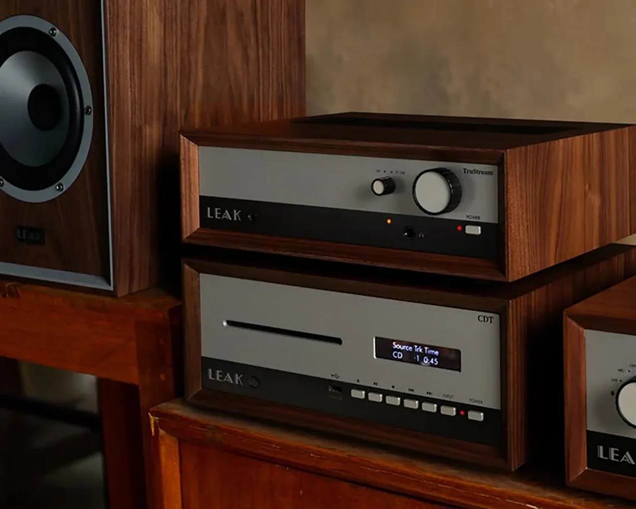 Wooden-cased LEAK audio amplifier and CD player stacked on a wooden cabinet next to a speaker.