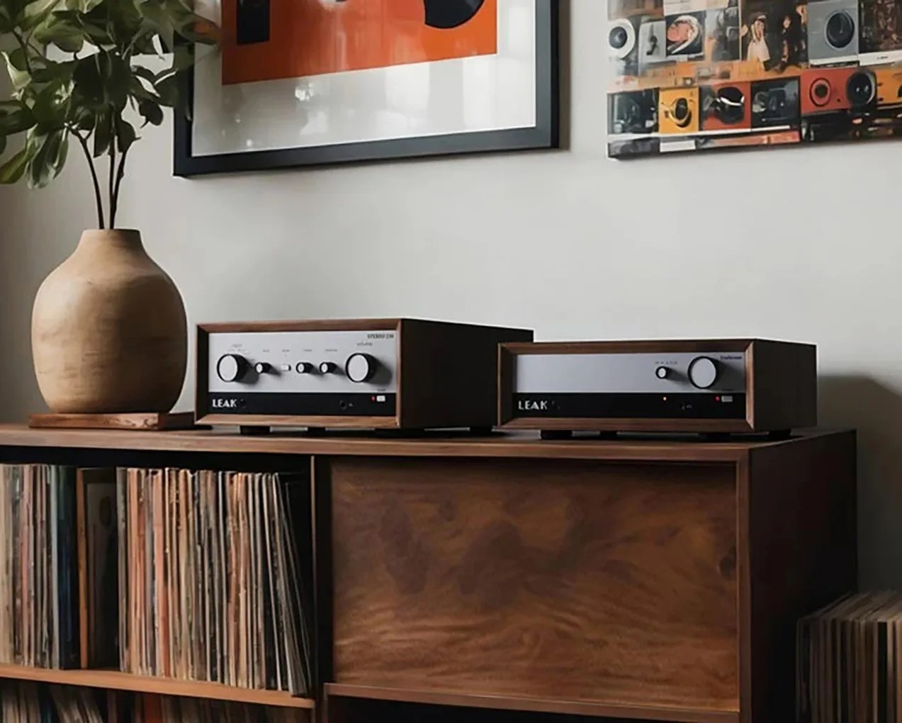 Wooden audio equipment with silver and black front panels labeled "LEAK" on a wooden shelf with vinyl records and a large ceramic vase.