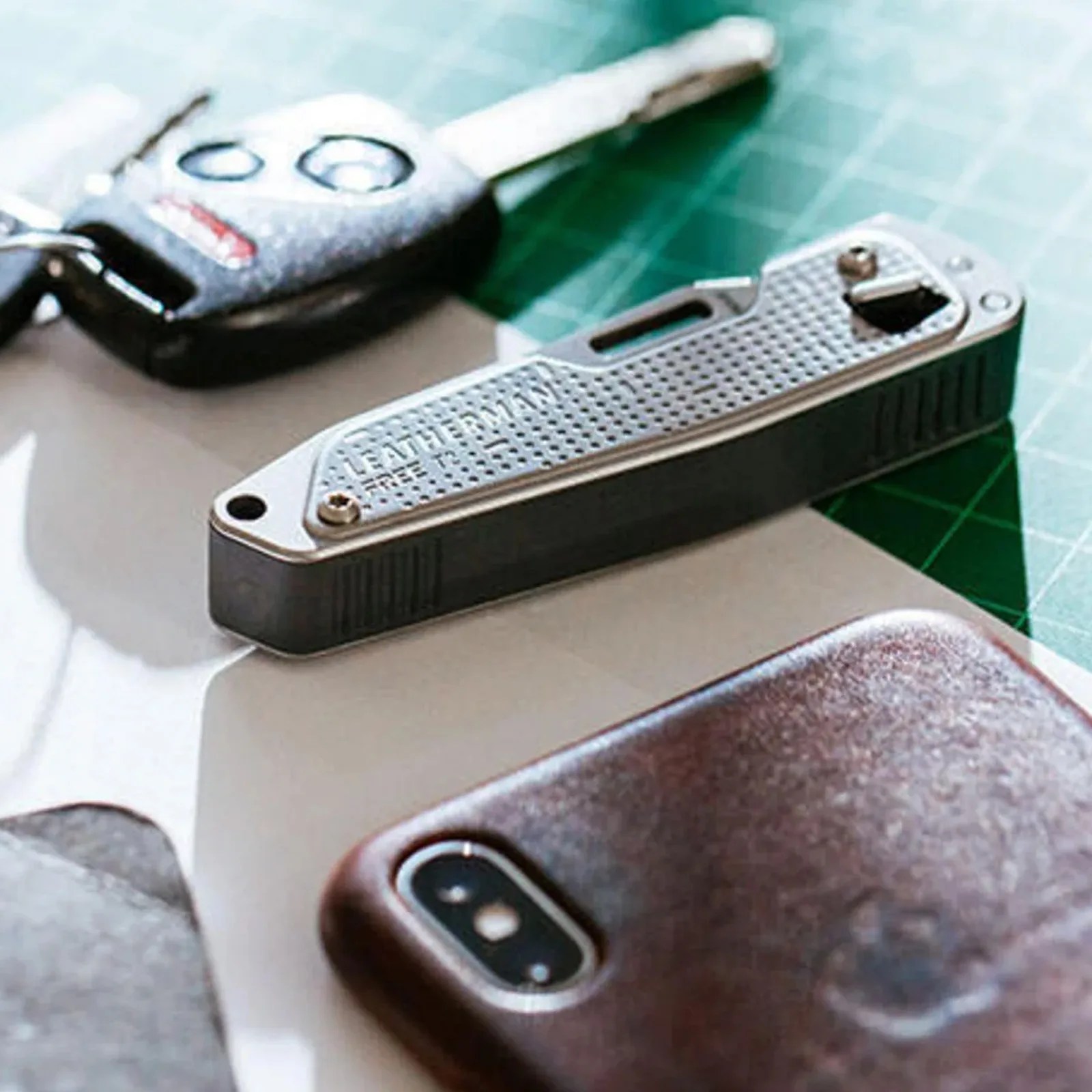 Silver Leatherman Free P2 multi-tool next to a car key and a smartphone with a brown leather case.