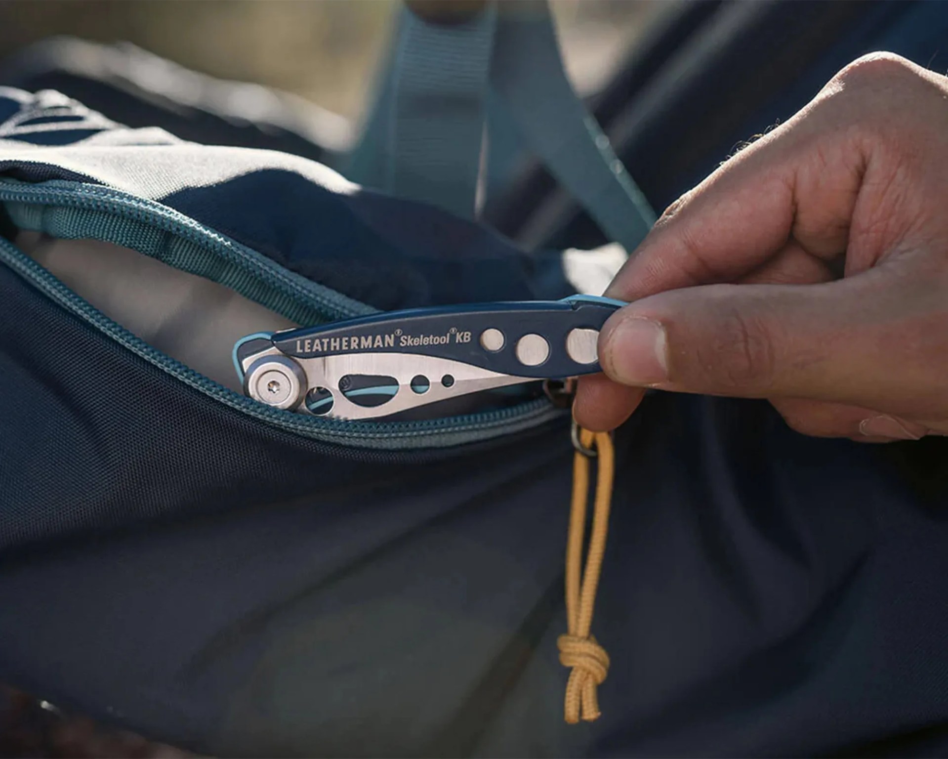 Hand holding a closed Leatherman Skeletool KB multitool partially inside a dark blue zippered bag.