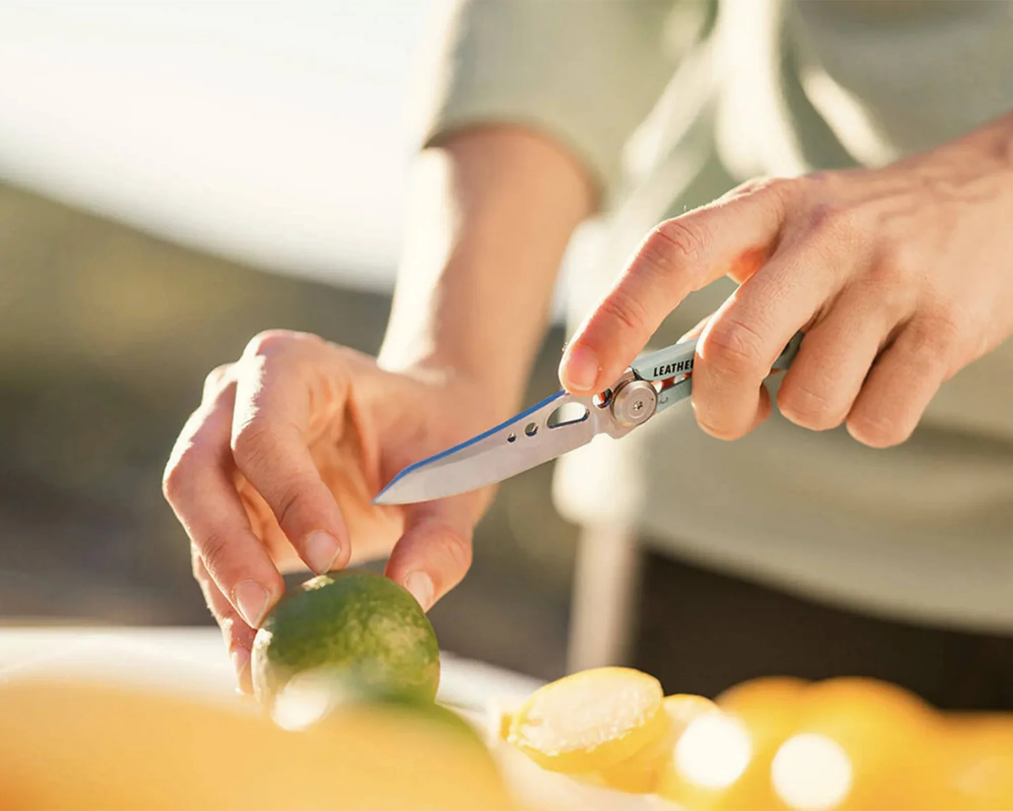 Person holding a folding knife with a silver blade and cutting a green lime.